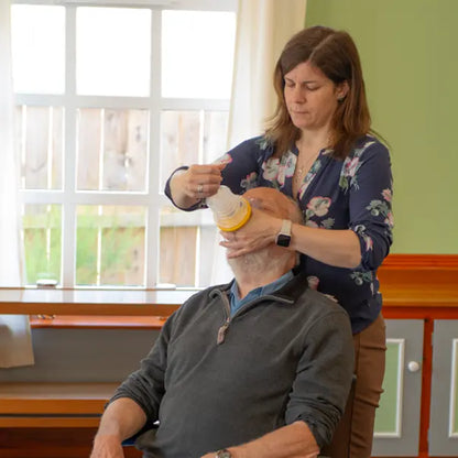 Woman using breathing apparatus on an elderly man's mouth in a home setting.