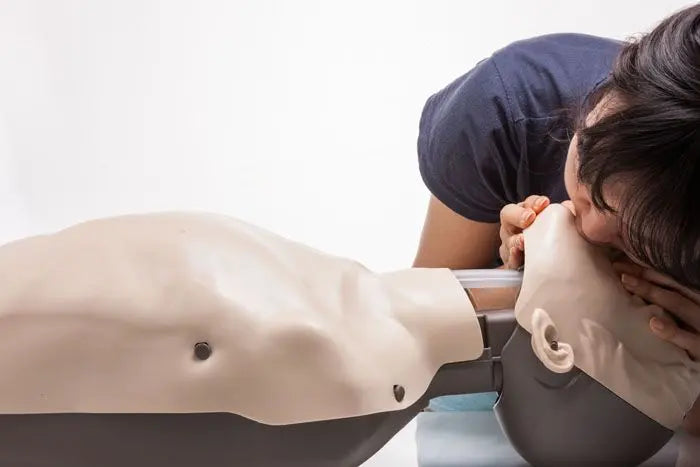 Person performing CPR on a mannequin with a white background