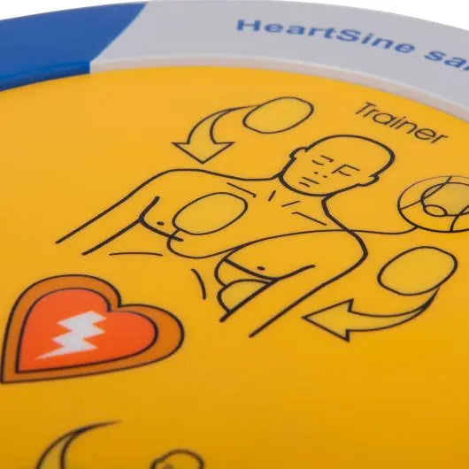 HeartSine AED trainer device with instructional diagram on a yellow background