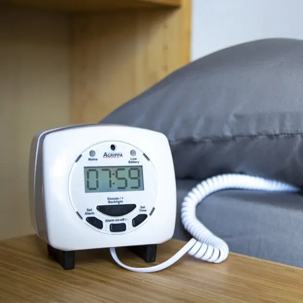 Digital alarm clock with a coiled cord on a wooden surface, with a blurred background.