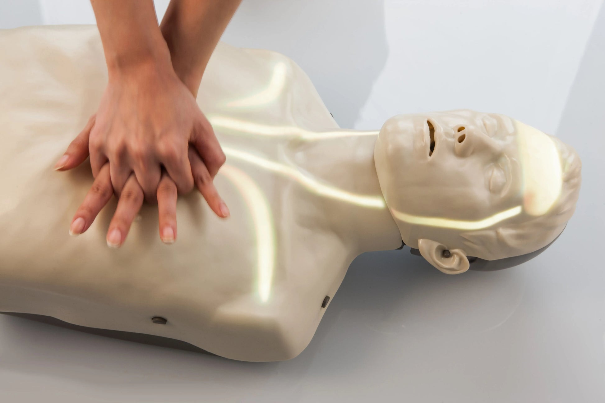Person performing CPR on a mannequin with hands on chest on a light background
