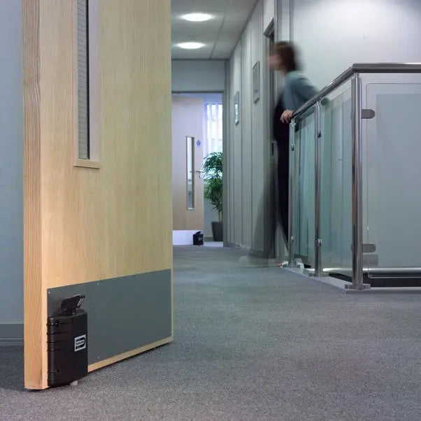 Person walking through a modern office hallway with glass walls and wooden doors.