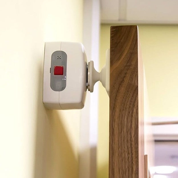 Wall-mounted security device with a red button on a white wall.